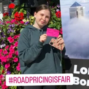 Woman holds red post-it note. It reads: "Road pricing [tick]". Banner over photo reads "#roadpricingisfair